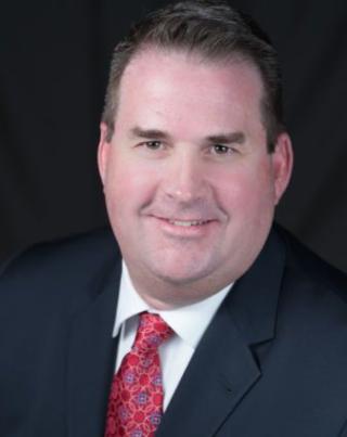 a man wearing a suit and tie smiling at the camera