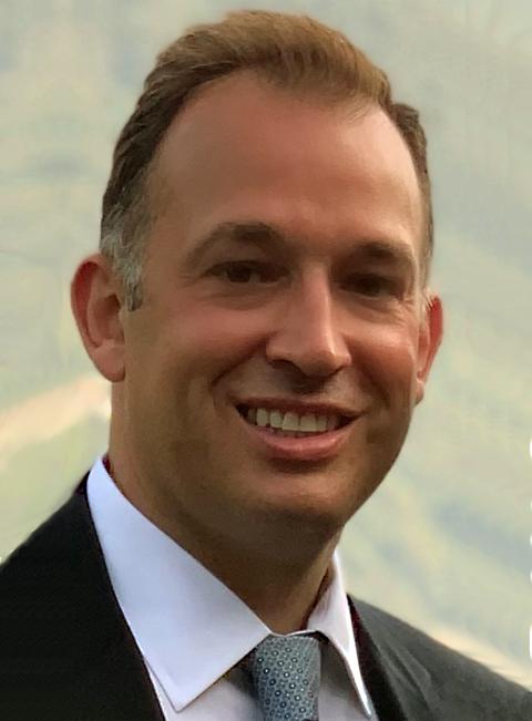 a man wearing a suit and tie smiling and looking at the camera