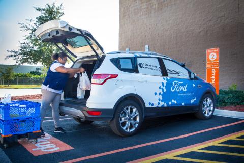 a person standing in front of a blue car parked in a parking lot