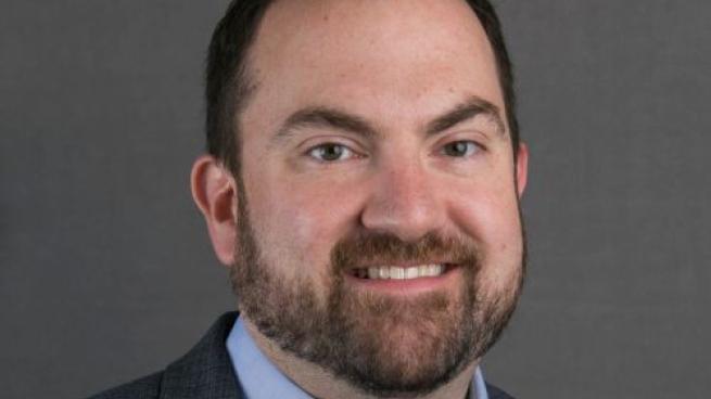 a man wearing a suit and tie smiling at the camera