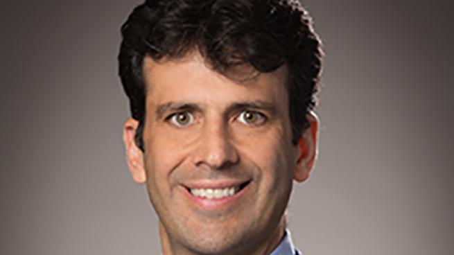 a man wearing a suit and tie smiling and looking at the camera