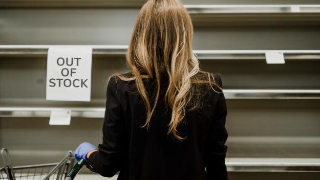 Woman looking at empty shelves with out of stock sign